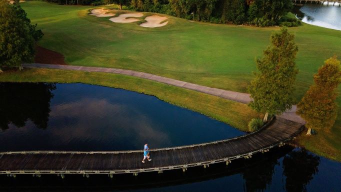 A man walking on a bridge over a body of water at a golf course in Orlando, Florida