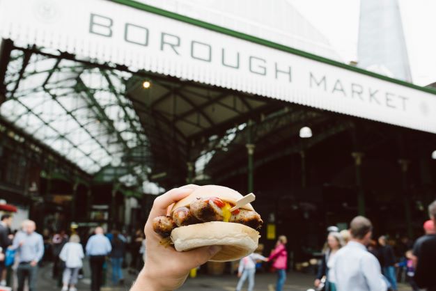 A hand holds up a burger in front of Borough Market in London, England, United Kingdom