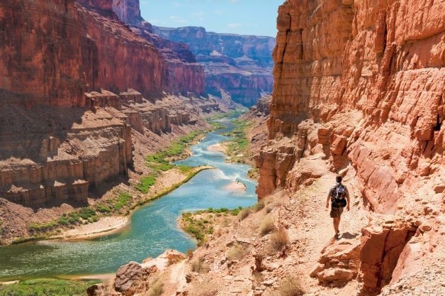 A hiker walking on a trail through the Grand Canyon near the Colorado River