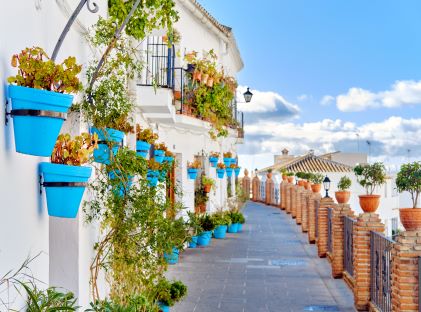 An empty street of white, stucco buildings with blue plant pots on a sunny day in Costa del Sol, Andalusia, Province of Málaga, Spain
