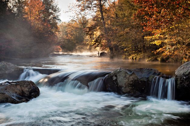 An angler fishing on the banks of a stream in the Great Smoky Mountains National Park in Tennessee with fall foliage