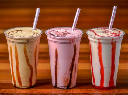 Three milkshakes with straws on a wooden table