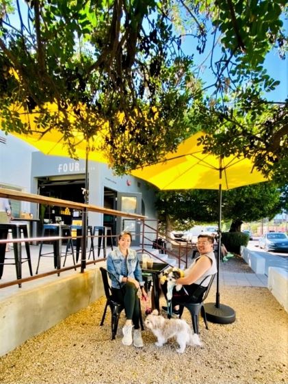 Hilton Grand Vacations Owner Raeanne sit in outdoor seating under a yellow umbrella in Old Town Scottsdale, Arizona, with her two dogs