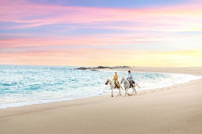Idyllic scene, couple horseback riding shoreside, sunset painted skies overhead, Los Cabos, Mexico. 