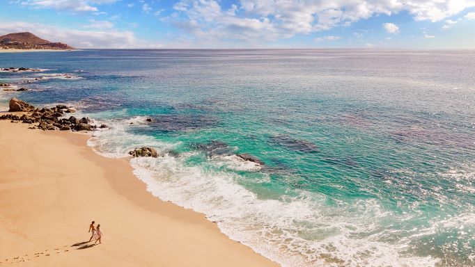 Aerial view, couple strolling a tropical beach, blue skies overhead, Los Cabos, Mexico.