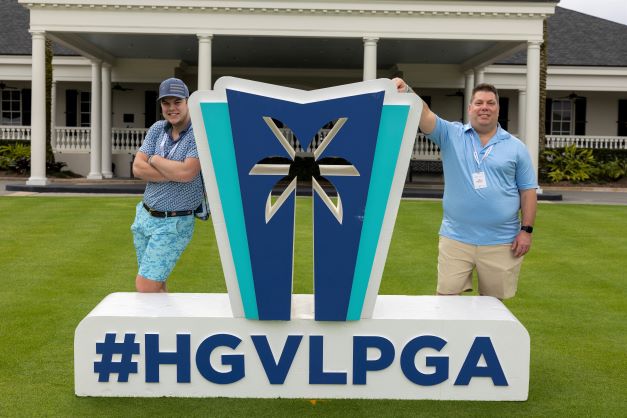 Hilton Grand Vacations Owners pose together by a sign with the palm tree logo of the HGV Tournament of Champions and the hashtag #HGVLPGA