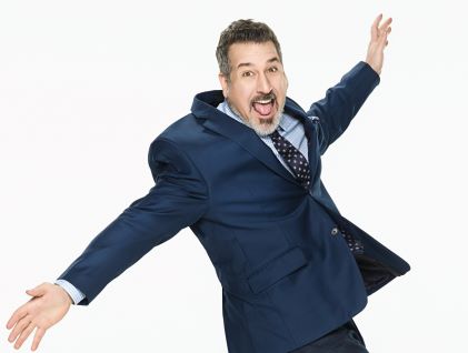 Joey Fatone, a Hilton Grand Vacations celebrity Brand Ambassador, in a blue suit and arms outstretched