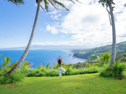 A young woman practices yoga overlook a tropical coastline