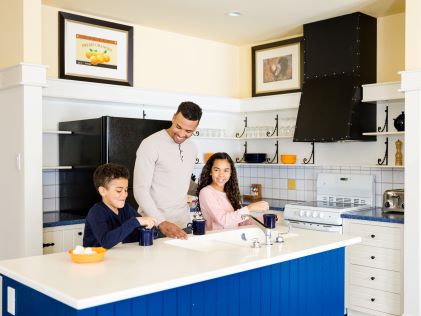 A parent and two kids making hot cocoa together in the in-Suite kitchen at Tremblant, a Hilton Grand Vacations Club in Quebec, Canada
