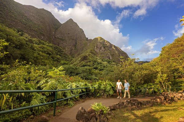 A gay couple holds hands while walking down a lush trail in Iao Valley in Maui, Hawaii