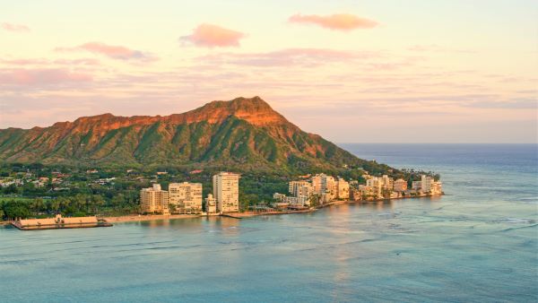 Modern buildings of Honolulu, Hawaii along the beaches of Oahu and Diamond Head in the background at sunset