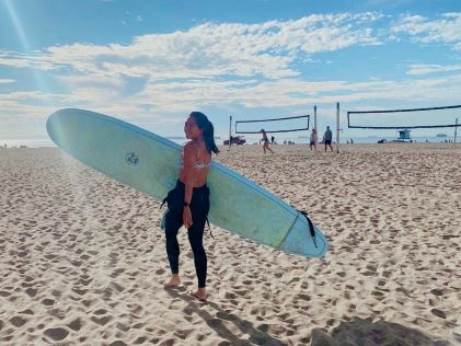 A Hilton Grand Vacations Owner holding a surfboard on Huntington Beach, California