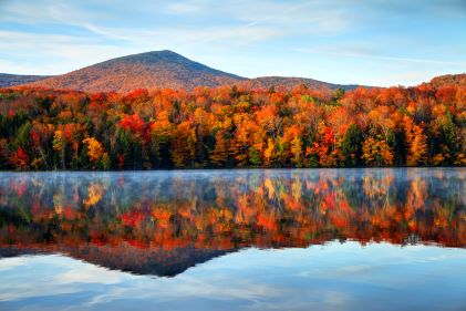 Beautiful image, fall foliage, placid lake, mountains in the distance, blue skies, Vermont. 