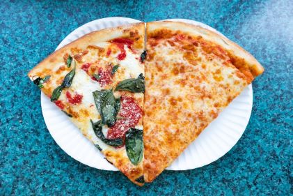 Flat lay image, classic New York City-style pizza slices, white paper plate, blue counter, NYC street food. 