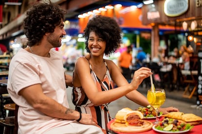 A man and a woman sit at a table with food and drinks at an outdoor market