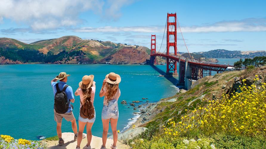 Three people enjoy the view from a hill overlooking the Golden Gate Bridge, San Francisco, California