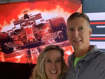 A Hilton Grand Vacations Member and her partner stand in front of a race digital sign at a Formula 1 event in Las Vegas, Nevada