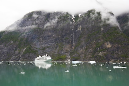 Cruise ship sails under mountain cloud along the stunning Alaskan coastline