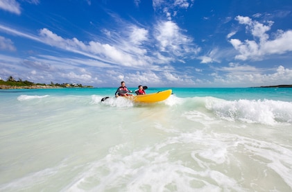 Father and son in a yellow kayak catch a wave in a tropical ocean