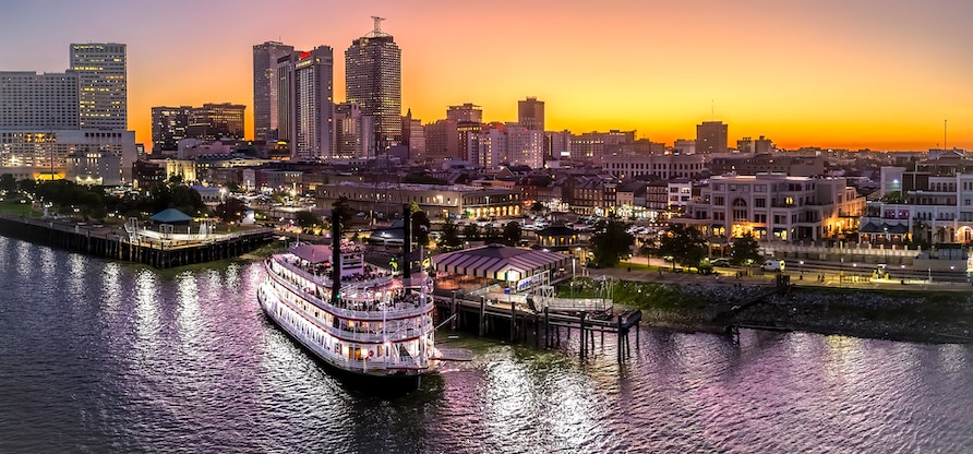 A large steamboat sets sail at sunset on the Mississippi River in downtown New Orleans, Louisiana