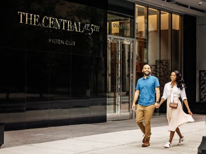 A couple holding hands walks by the entrance to The Central at 5th, a Hilton Club, one of Hilton Grand Vacations' New York timeshares