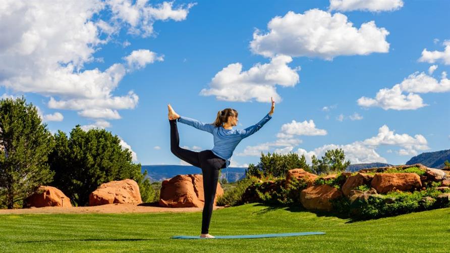 A woman practices yoga in a field in Sedona, Arizona, with red mountains in the background