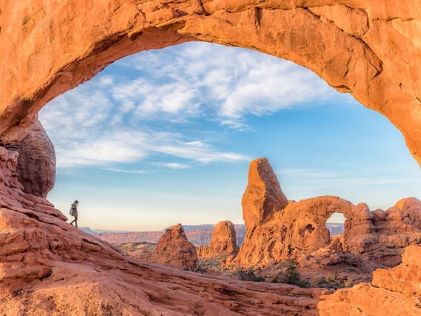 A hiker under a natural red sandstone arch in southern Utah