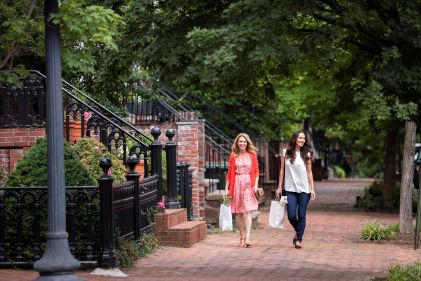 Two women strolling along brick-lined historic street with shopping bags, Washington, D.C.