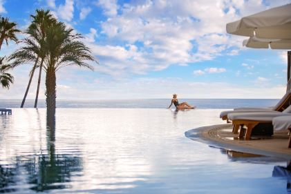 Stunning resort pool scene, woman lounging on edge of infinity pool, clear blue skies, La Pacifica Los Cabos, a Hilton Club, Mexico. 