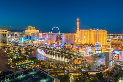 Long shot of the Las Vegas Strip just after dusk. Bright lights and attractions dot the skyline with a warm glow.
