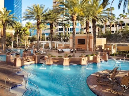 Long shot of the pool at The Boulevard, a Hilton Grand Vacations Club, under sunny skies. features crystal blue waters, lush palms and landscaped grounds.