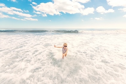 Happy child playing in wide expanse of South Carolina ocean shore as waves move in slow motion.