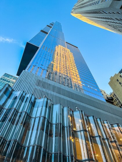 Stunning image looking straight up at Central Park Towers in New York City's Billionaire's Row. The tower's mirrored surface reflects surrounding buildings under clear blue skies.
