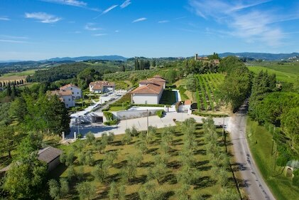 Aerial view overlooking Tuscany hillsides and the Borgo alle Vigne, a Hilton Grand Vacations Resort, set under blue skies and surrounded by lush green vineyards and trees.