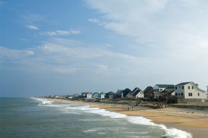 Cozy coastal scene, beach houses lining golden shoreline, overcast skies overhead, Kitty Hawk, North Carolina. 