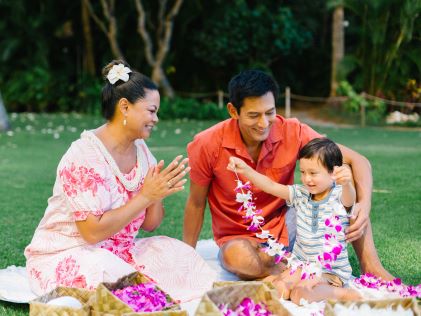 Two adults help a child make a lei in Hawaii
