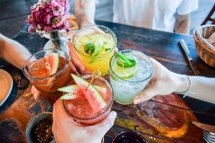 Close up of four hands holding colorful refreshing beverages garnished with fruit.
