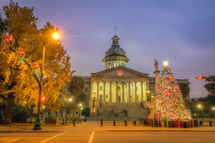 Winter scene with Christmas tree and lights in the foreground in front of the white and warmly-lit Charleston, SC state house.