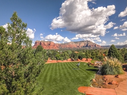 Peaceful landscapes of Sedona invite relaxation amidst a varied scene of green grass and red buttes in the distance.