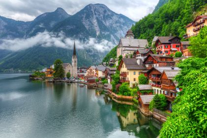 Picturesque alpine village perched along coast, lush greenery against winter sky, mountains in distance, Austria. 