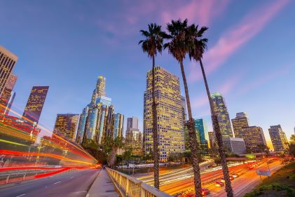 Artistically shot image, downtown buildings, palm trees, cars blurring by, dusk sky overhead, Los Angeles, California. 