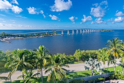Distant view of blue skies and surrounding water by Sanibel, Florida Causeway and tree-lined road in the foreground.