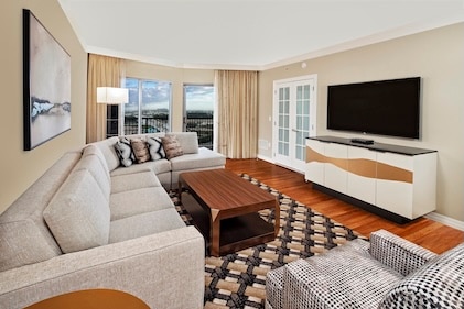 Interior view of a Suite at Parc Soleil, a Hilton Grand Vacation club in Orlando, showing the living room with large sofa, coffee table, Large TV, wood floors, and patio.