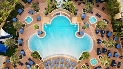Straight-on aerial view of the ornately-shaped pool and surrounding patio with lounge chairs and umbrellas at Parc Soleil, a Hilton Vacation Club in Orlando. 