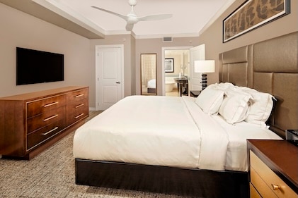 Image of bedroom in Parc Soleil, a Hilton Vacation Club featuring a bed with crisp, white linens, dark wood base, leather headboard, and warm wood furnishings.