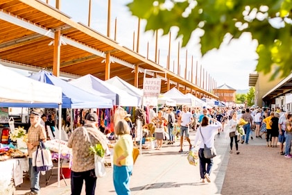Vendors line the path of the Santa Fe Farmer's Market in the Railyard Arts District. The Railyard sign is in the distance with the mountains beyond.