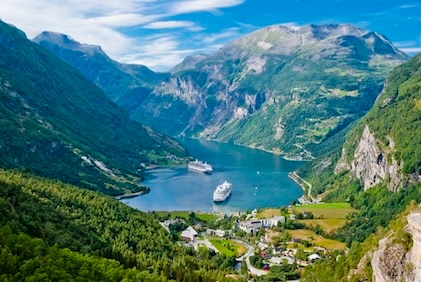 Aerial view of Norway Fjords surrounding a body of water with cruise ships. The fjords are tall and green against a blue sky.