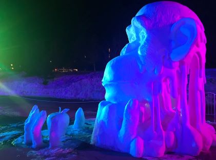 A snow sculpture of a monkey at night, illuminated by colored lights