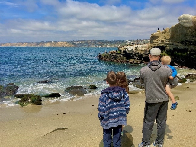 Father and kids looking out to the Pacific Ocean in a San Diego beach. 