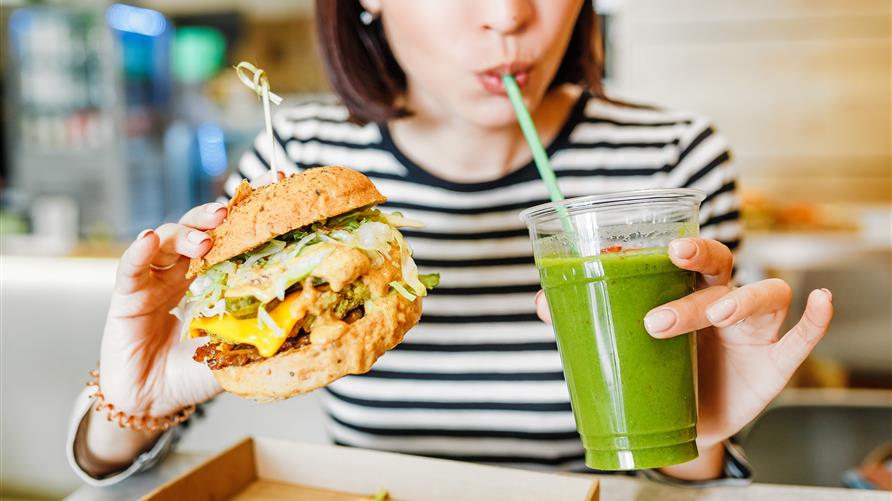 Woman eating a vegan burger and drinking green juice. 